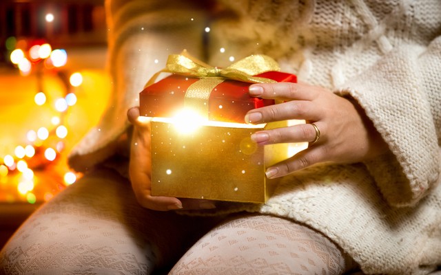 Closeup photo of young woman opening gift box with light coming out of it